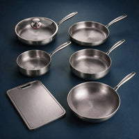 Pannenset van vijf handgehamerde titanium pannen, waarvan één met glazen deksel, met een metalen snijplank op een donkerblauwe achtergrond