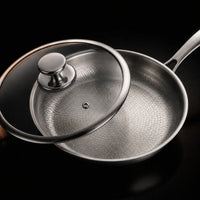 Close-up van een titanium koekenpan met de glazen deksel er schuin op