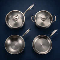 De titanium basis-keukenset van bovenaf gezien: twee pannen met glazen deksel, een wokpan en een koekenpan