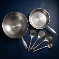 Titanium wok, koekenpan en vier stuks keukengerei van bovenaf gezien op een donkerblauwe achtergrond