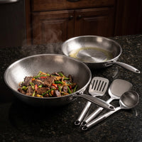 Titanium wok met roerbakgerecht van rundvlees en groente op een granieten aanrecht, met de koekenpan en het keukengerei ernaast