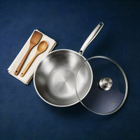 Titanium wok van bovenaf, met glazen deksel en een houten spatel en lepel op een servet