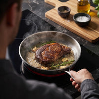 Steak met rozemarijn en knoflook in de titanium koekenpan op een inductiekookplaat, van bovenaf gezien