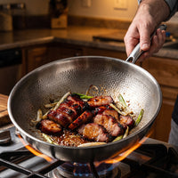 Geglaceerde stukken vlees met lente-ui in de titanium wok op een gasfornuis, een hand houdt de greep vast