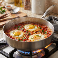Shakshuka met drie eieren in tomatensaus in de titanium pan met hoge rand op een gasfornuis