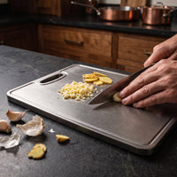 Hand snijdt gember en knoflook met een koksmes op de titanium snijplank
