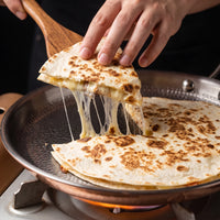 Hand tilt een punt quesadilla met draden gesmolten kaas uit de titanium crêpepan