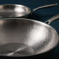 Close-up van de gehamerde binnenkant van de titanium wok, met de koekenpan op de achtergrond