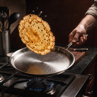 Pannenkoek wordt in de lucht gekeerd boven de titanium crêpepan