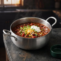 Chili con carne met zure room, geraspte kaas en lente-ui in de diepe titanium kookpan op een stenen aanrecht