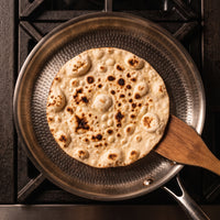 Platbrood met een houten spatel in de titanium crêpepan, van bovenaf gezien