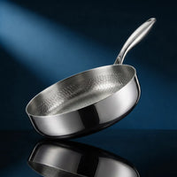Handgehamerde titanium pan met hoge rand 10 inch, schuin geplaatst op een donkerblauwe achtergrond