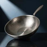 Handgehamerde titanium wok 12 inch, schuin geplaatst op een donkerblauwe achtergrond