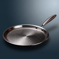 Handgehamerde titanium crêpepan 11 inch met lage rand, schuin geplaatst op een blauwgrijze achtergrond